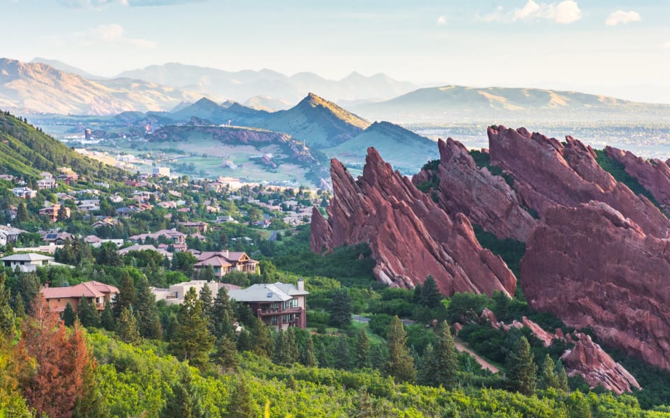 Red sandstone rock formations rising above luxury homes and pine forest in Roxborough, a south Denver suburb in Colorado, with the foothills in the background